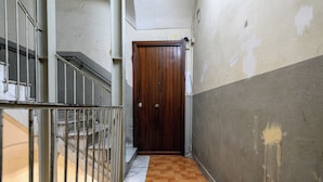 Un couloir étroit avec une porte en bois, une rambarde en métal et un sol carrelé.