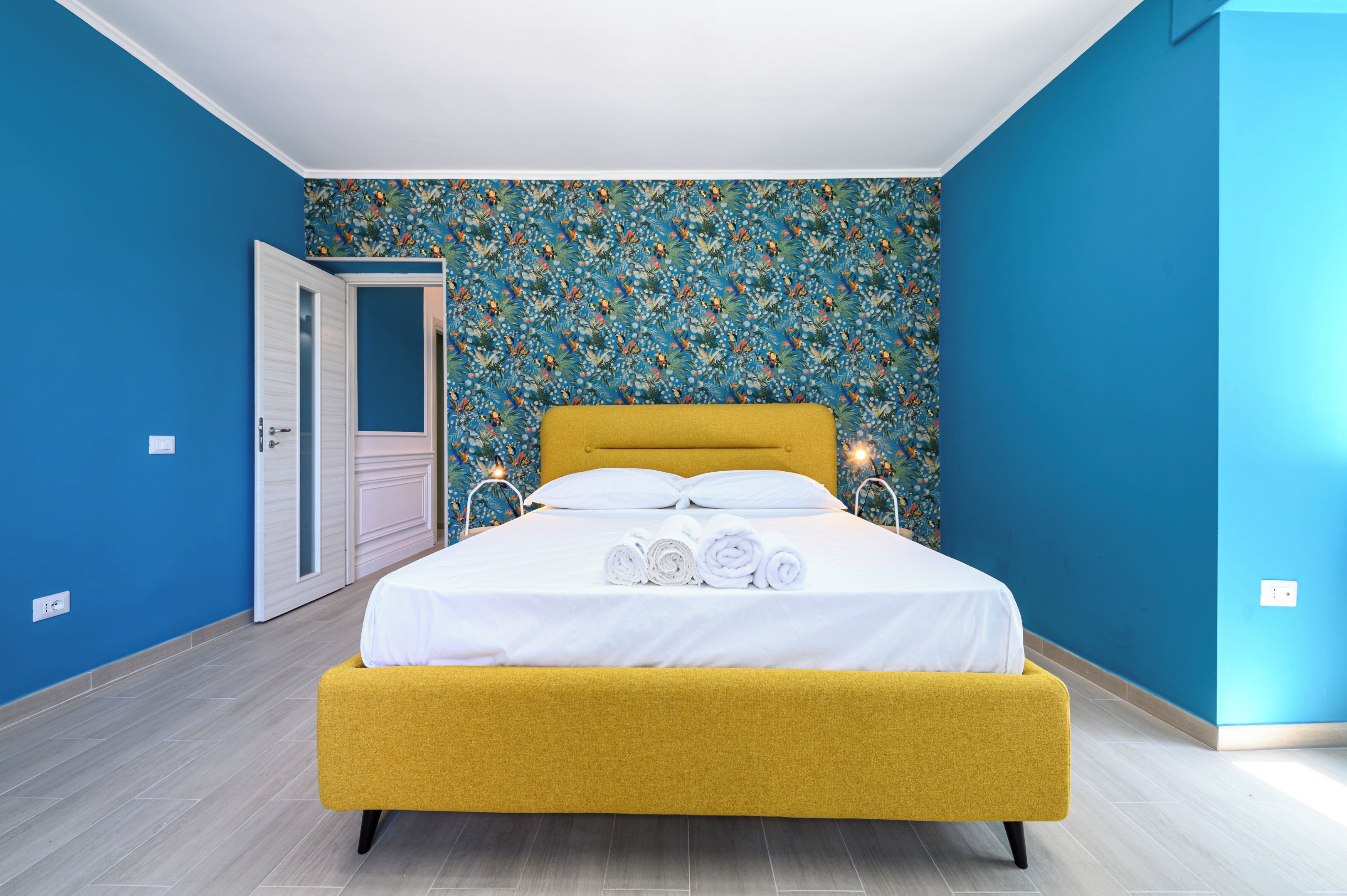 A bedroom with a yellow bed, white bedding, and a floral-patterned wall.