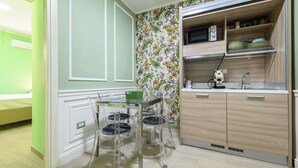 Une cuisine compacte équipée d’un four à micro-ondes, d’un évier et de meubles en bois. Un petit coin repas est aménagé avec une table et des chaises en verre.