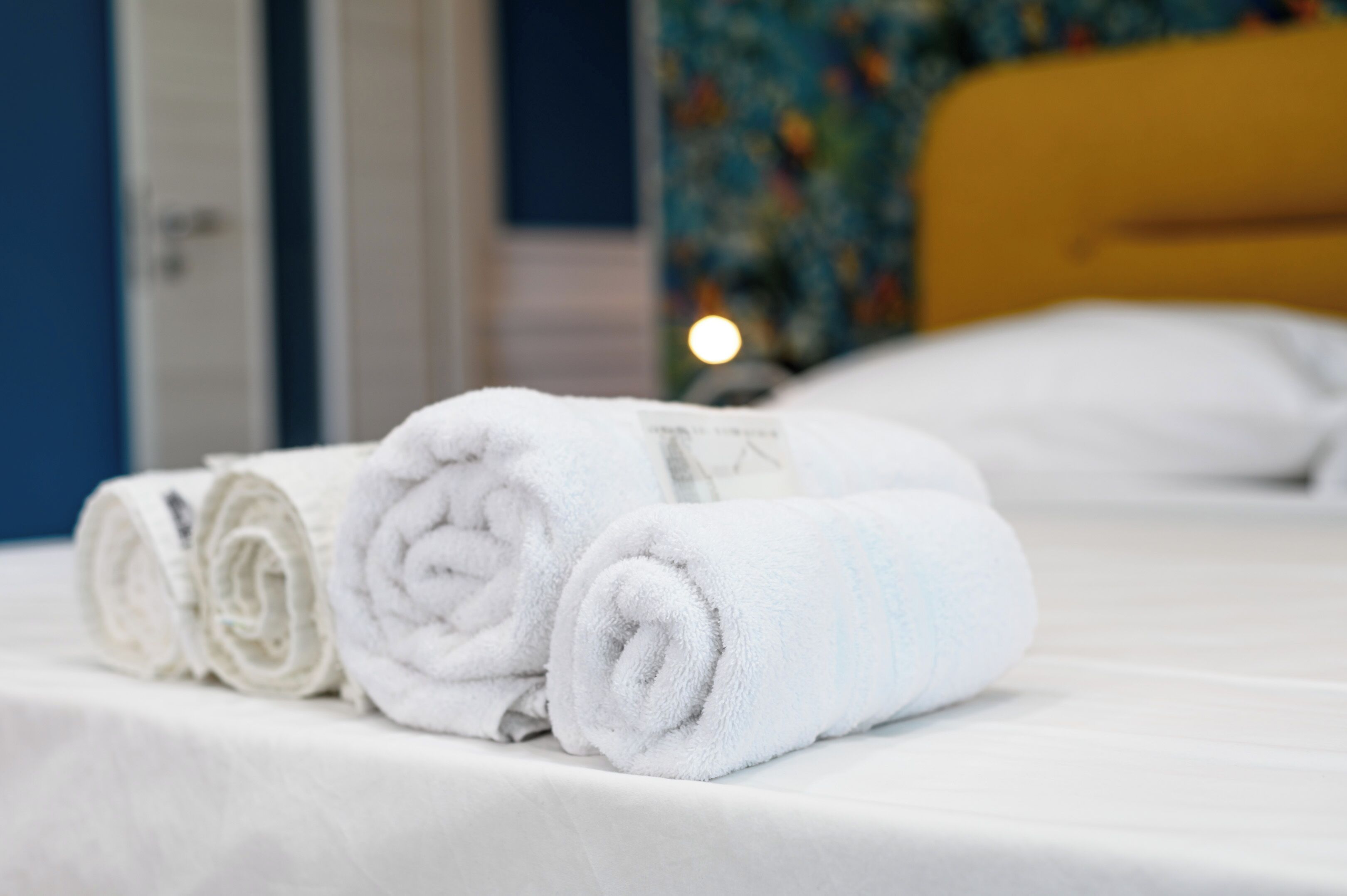 Una cama bien tendida con toallas blancas y un cabecero amarillo.