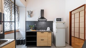 Une cuisine moderne équipée d’une cuisinière, d’un four à micro-ondes et d’un réfrigérateur intégrés. Une fenêtre ornée de motifs en fer forgé et une porte coulissante au design traditionnel complètent l’ensemble.