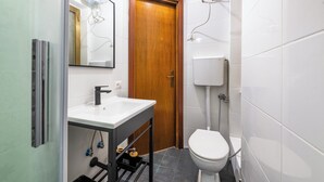 Une petite salle de bain avec un lavabo blanc, une porte en bois, des toilettes et un miroir.