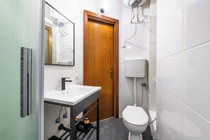 A compact bathroom with a white sink, a wooden door, a toilet, and a mirror. - Gianicolense Apartment (Rome)