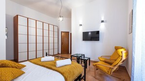 Une chambre d’hôtel avec un lit, un fauteuil jaune, une télévision et une porte coulissante.