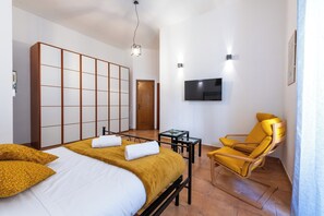 A hotel room with a bed, a yellow armchair, a TV, and a sliding door. - Gianicolense Apartment (Rome)