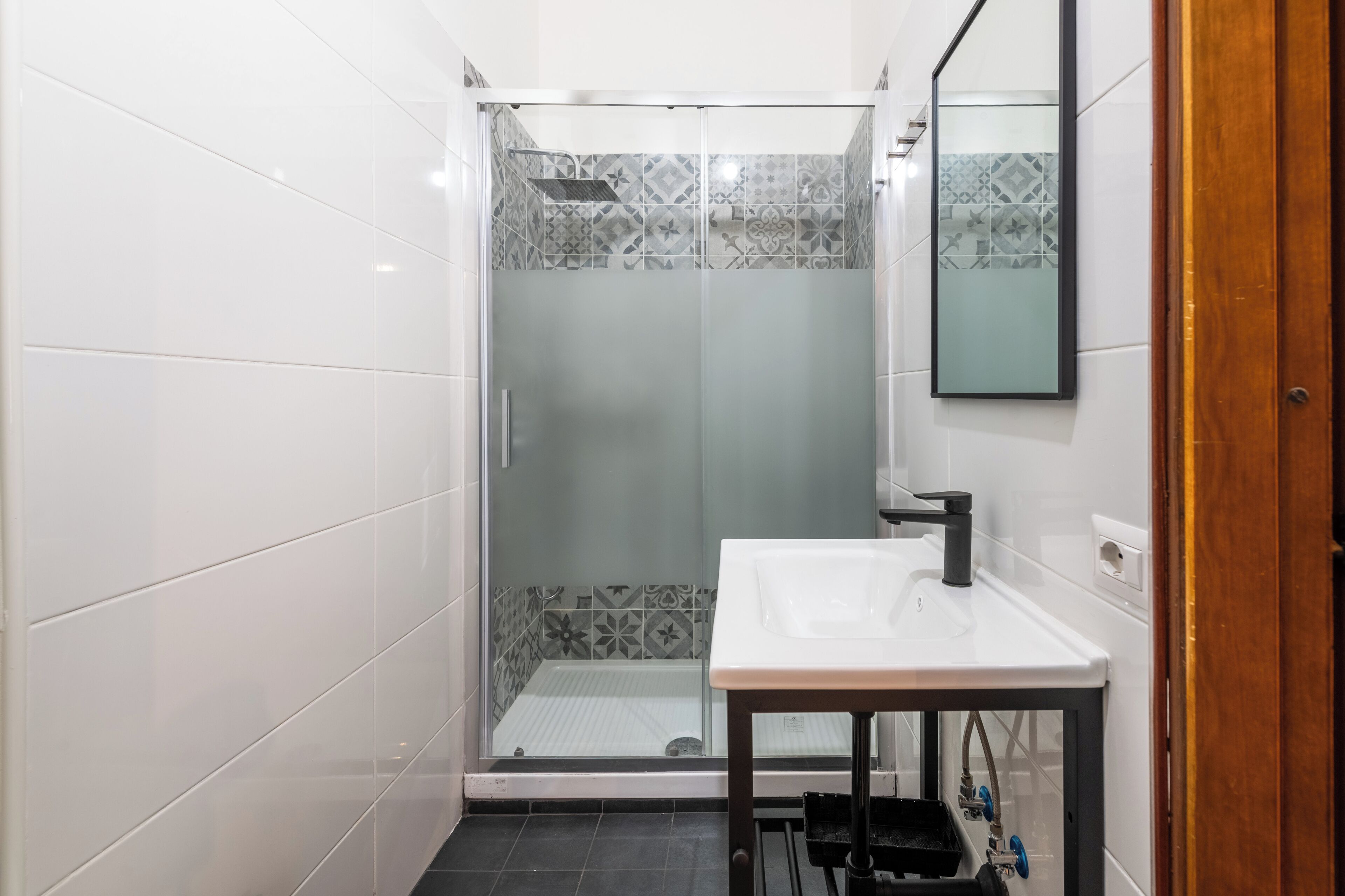 A modern bathroom with a glass-enclosed shower, a white sink with a black faucet, and patterned tiles on the walls.