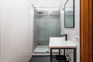 Une salle de bain moderne avec une douche à parois de verre, un lavabo blanc doté d’un robinet noir et des carreaux décoratifs sur les murs.
