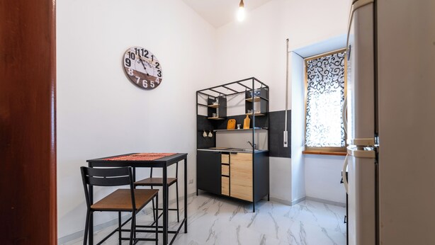 Une cuisine compacte dotée d’un évier intégré, d’une petite table à manger avec des chaises et d’une horloge murale décorative.