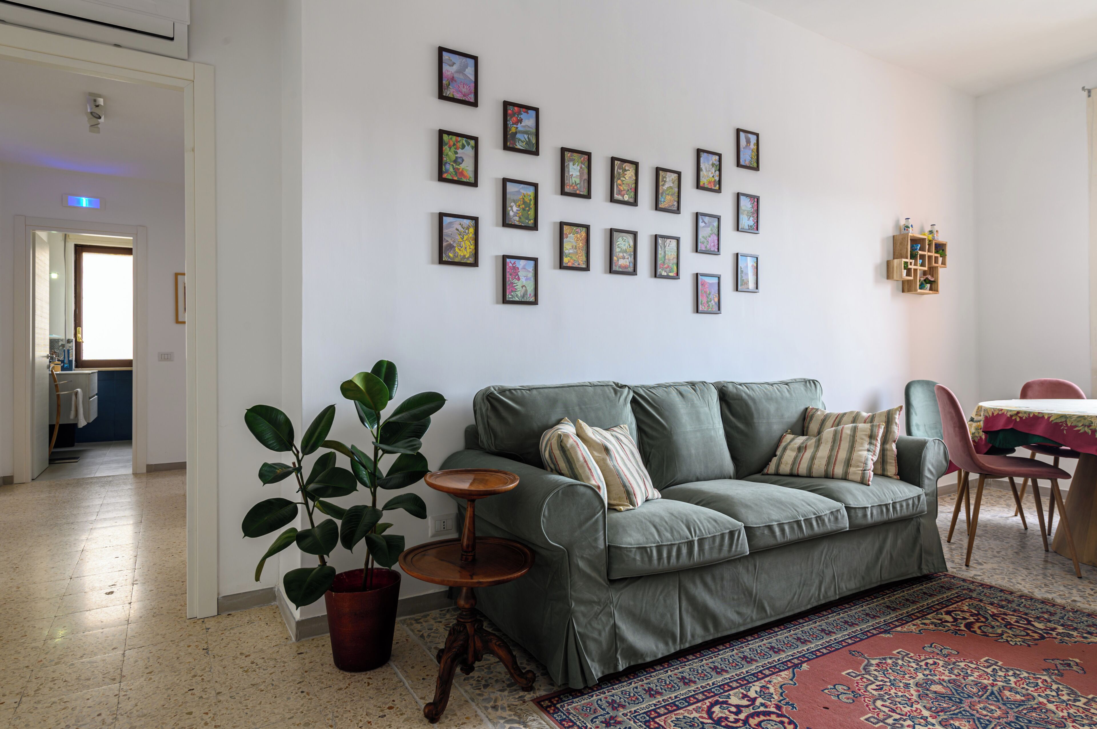 Un salon avec un canapé vert, une plante en pot, une petite table en bois et un tapis à motifs.