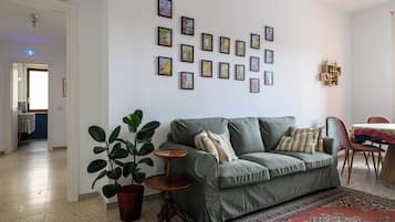 Un salon avec un canapé vert, une plante en pot, une petite table en bois et un tapis à motifs.