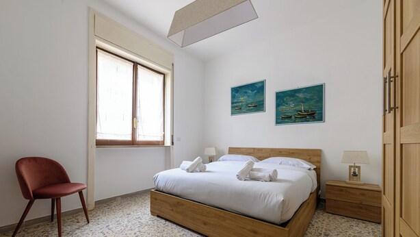 A bedroom with a wooden bed, a chair, a nightstand, and two paintings on the wall. - Via Coriolano 8 (Naples)