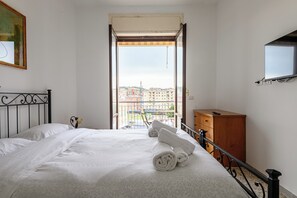 Quarto de hotel com cama, cômoda de madeira, televisão fixada na parede e varanda com vista para a cidade.