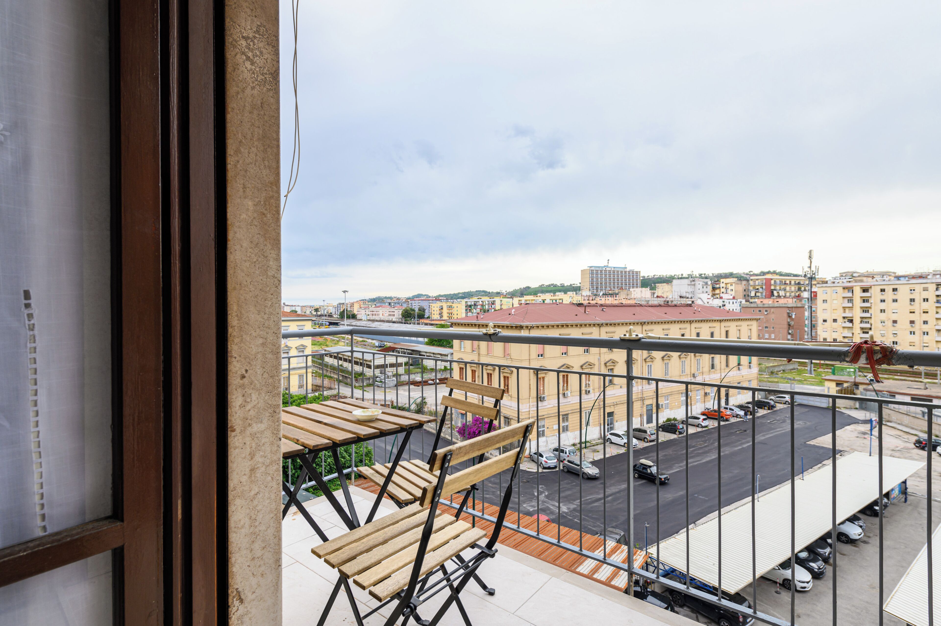 A balcony with a view of a cityscape, including buildings and a parking lot.