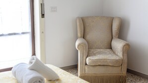 A room with a patterned bedspread, a rolled white towel, and a beige armchair with a patterned fabric. - Via Coriolano 8 (Naples)