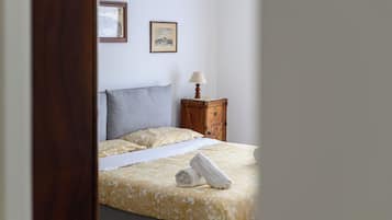 Un lit bien fait, avec une couvre-lit à motifs et des oreillers, une table de chevet avec une lampe, et deux tableaux encadrés accrochés au mur.