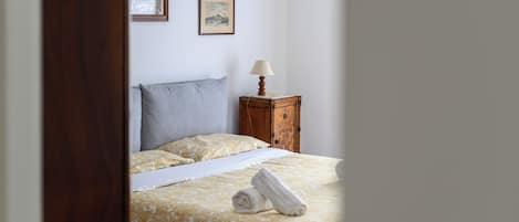 Una cama bien hecha con una colcha estampada y almohadas, una mesita de noche con una lámpara y dos cuadros en la pared.