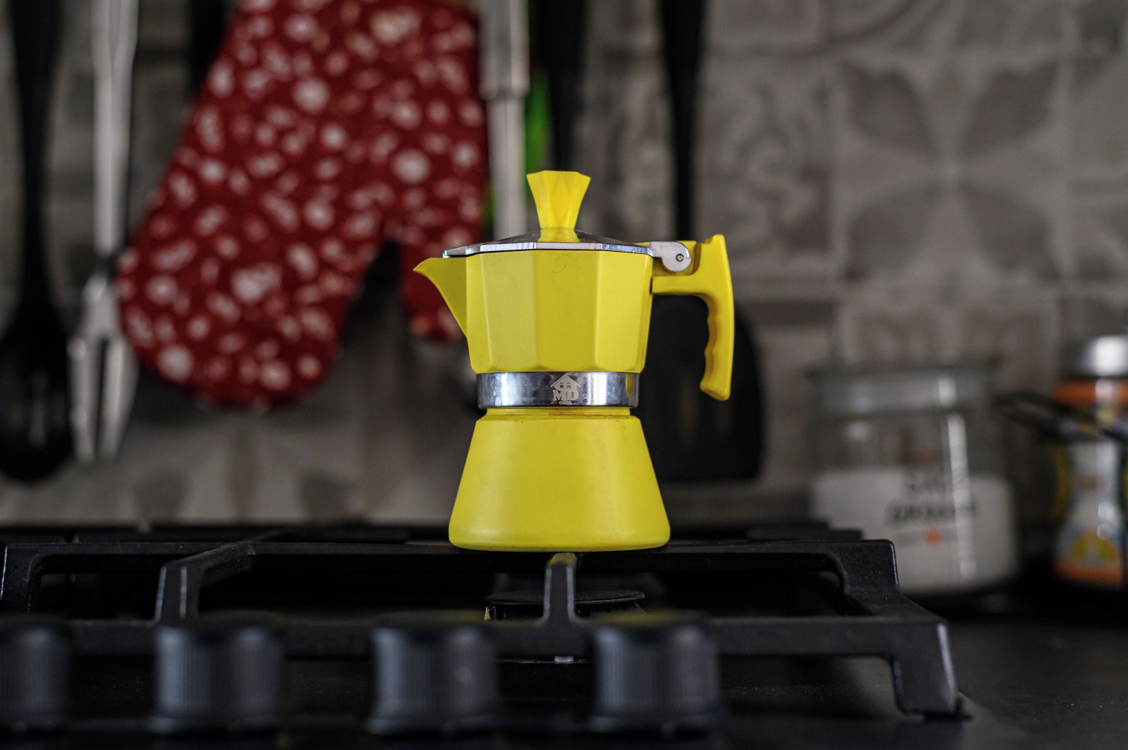 A yellow coffee maker on a stove.