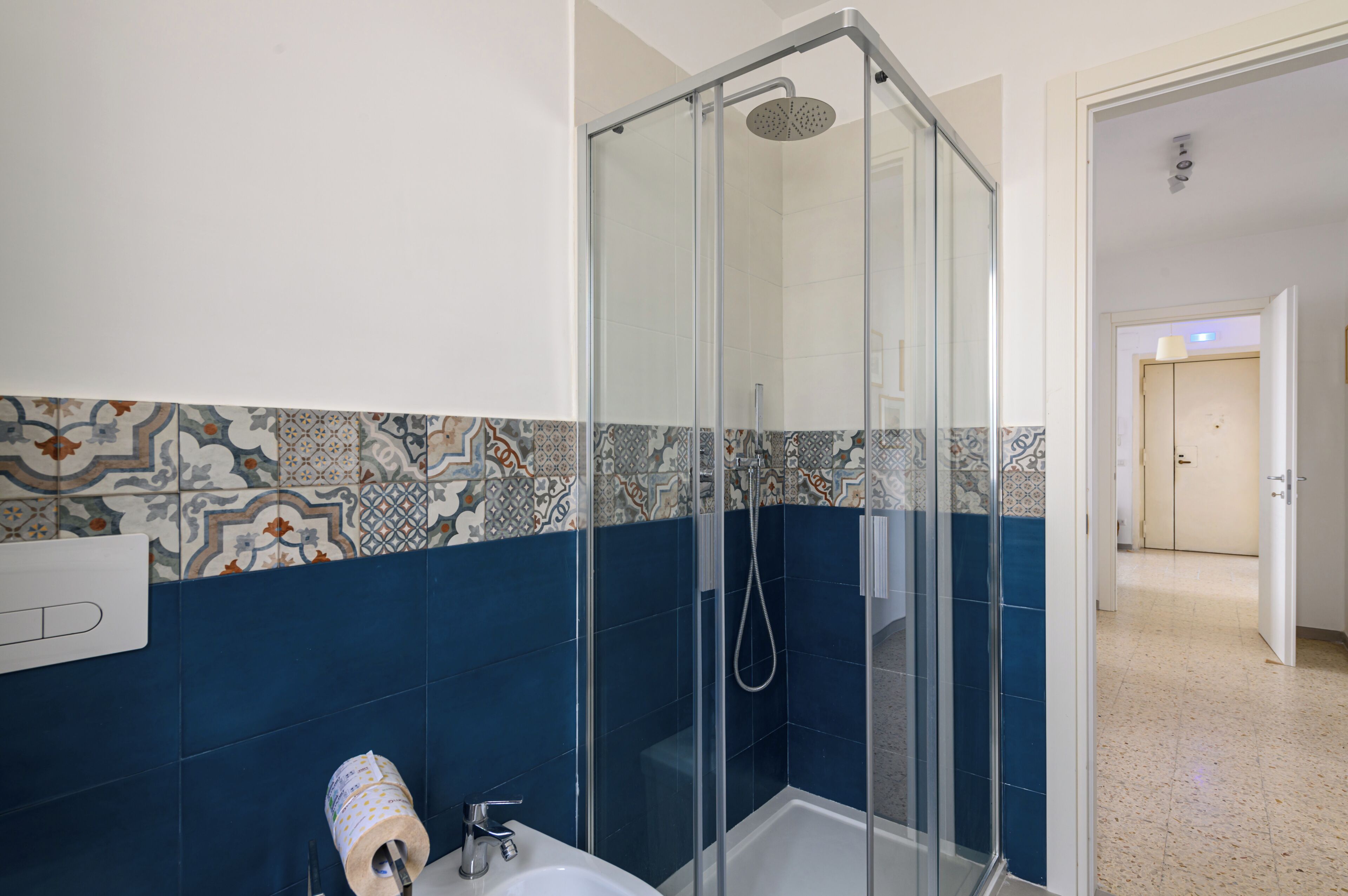 A bathroom with a glass-enclosed shower, a sink, and patterned tiles.