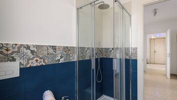 A bathroom with a glass-enclosed shower, a sink, and patterned tiles.