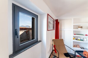 A room with a window, a chair, a shelf with decorative items, and a framed picture on the wall. - Purgatorio Terrace (Naples)