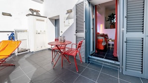 Eine kleine Terrasse mit Tisch und Stühlen, eine Tür zu einem Innenraum und ein Blumentopf.