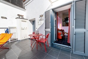 Eine kleine Terrasse mit Tisch und Stühlen, eine Tür zu einem Innenraum und ein Blumentopf.