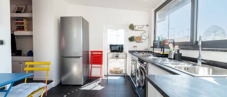 A modern kitchen with a stainless steel refrigerator, a red chair, and a blue table.