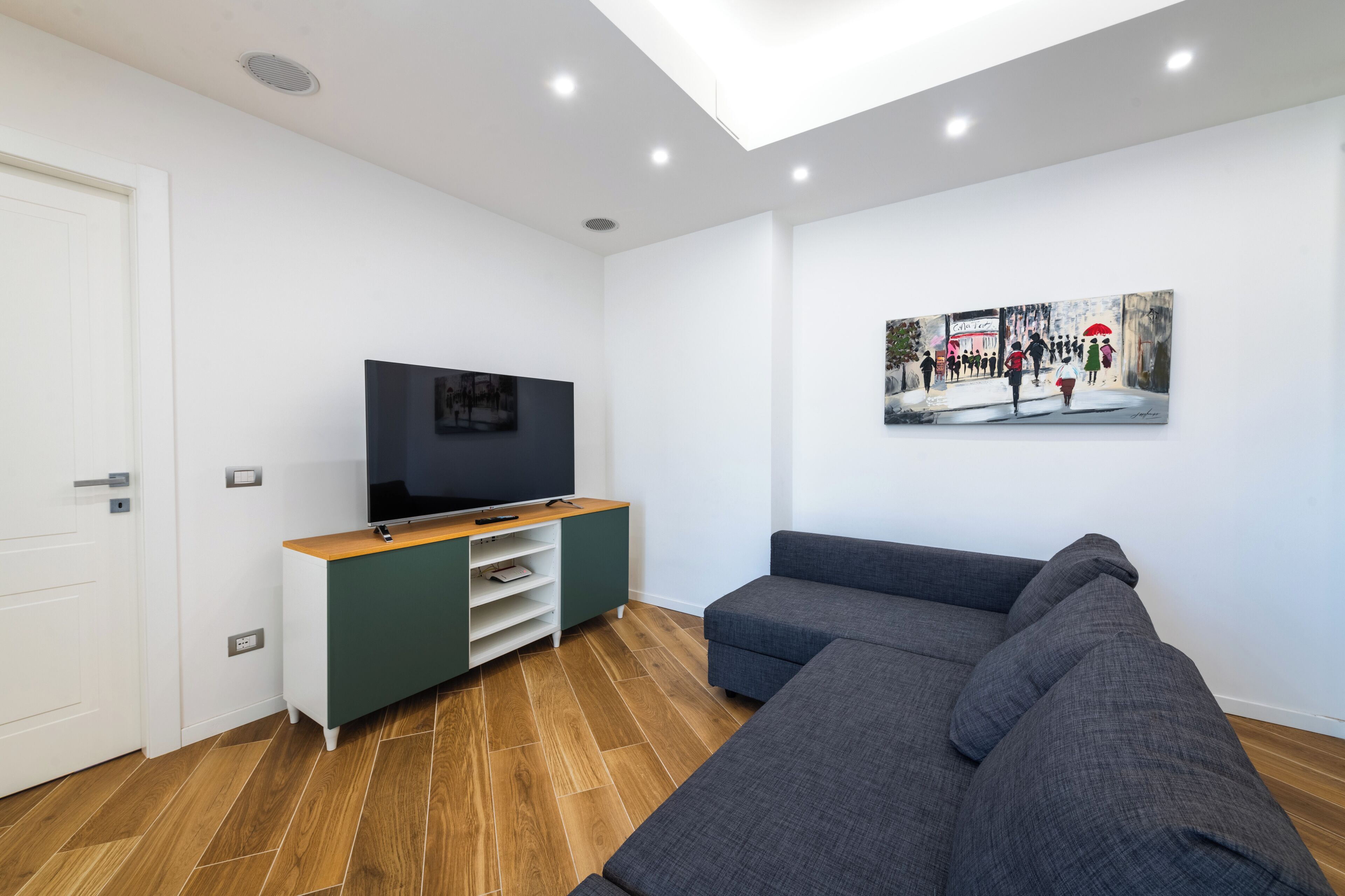 A modern living room with a grey sectional sofa, a flat-screen TV on a wooden TV stand, and a painting on the wall.