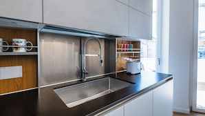 Une cuisine moderne dotée d’un évier en acier inoxydable, d’étagères en bois et offrant une vue sur l’extérieur.