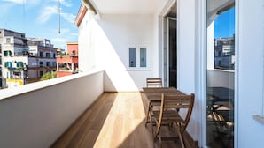 Un balcon avec une table et des chaises en bois, une vue sur le paysage urbain et une porte donnant sur un espace intérieur.