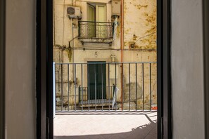 A view through a metal gate of a building with a balcony, a door, and a window. - A Tazzulella - Vico Graziella 12 (Naples)