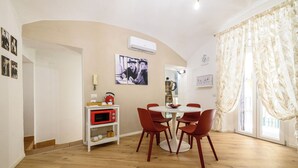 Uma área de refeições com uma mesa redonda e seis cadeiras vermelhas, uma prateleira branca com um micro-ondas vermelho, e um ar-condicionado fixado na parede.