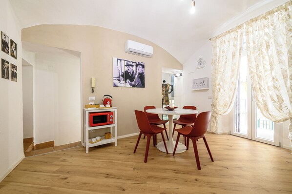 A dining area with a round table and six red chairs, a white shelf with a red microwave, and a wall-mounted air conditioner. - A Tazzulella - Vico Graziella 12 (Naples)