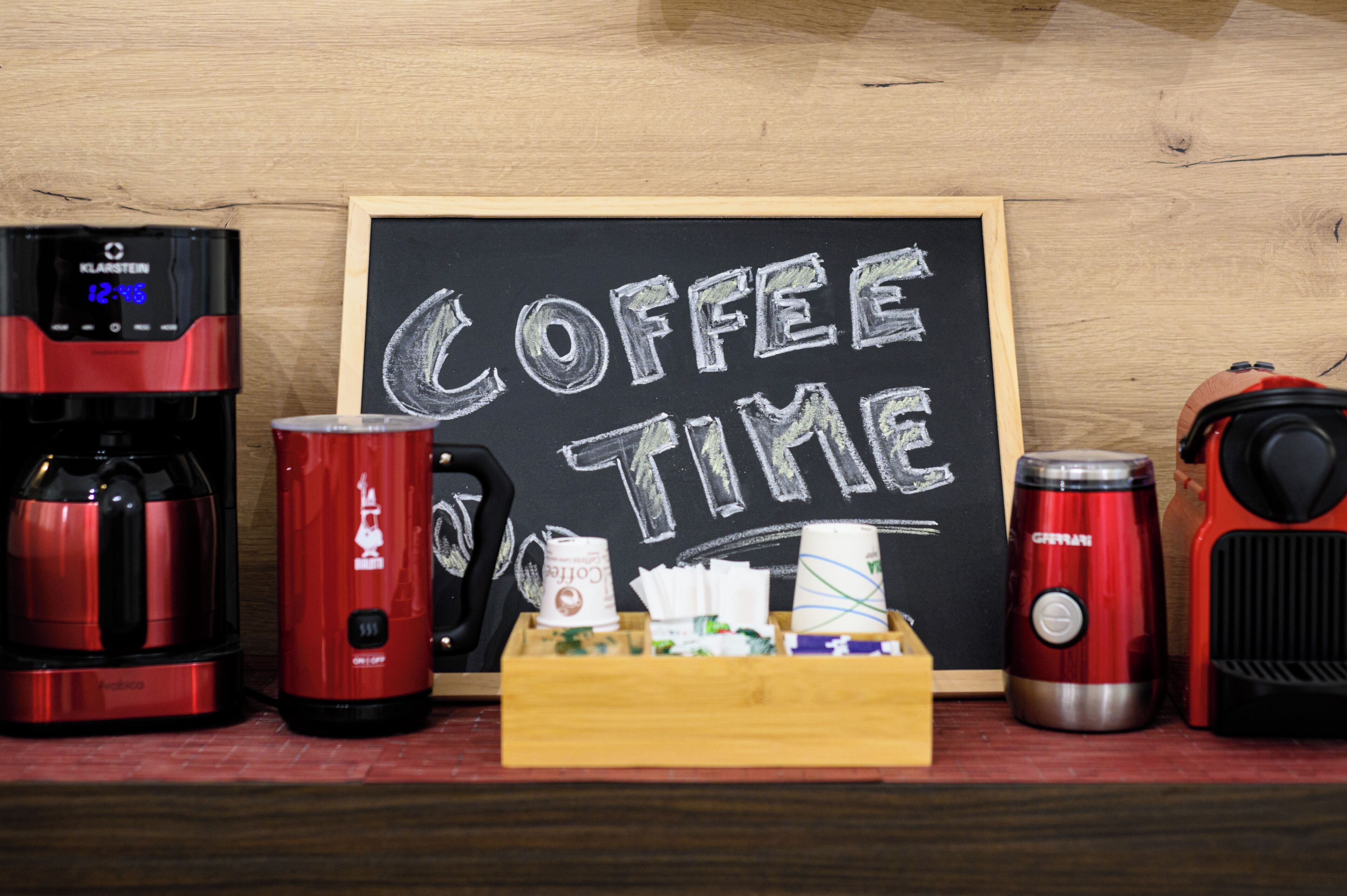 A coffee station with a coffee maker, a thermos, a mug, and a tray of coffee pods.