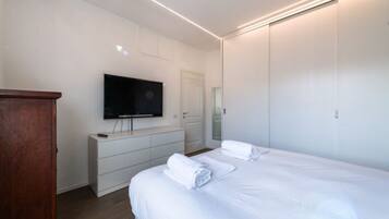 Quarto moderno com cama grande, televisão na parede, cómoda e guarda-roupa.