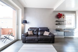 Uma sala de estar moderna com um sofá de couro escuro, um tapete branco e uma janela grande com vista para o exterior.
