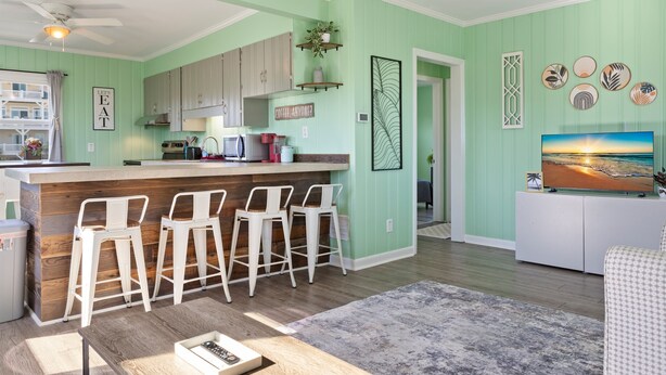 A kitchen with bar stools, a dining table, and a TV in a living area. - Close to beach, pier and restaurants (Surf City)