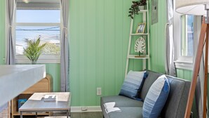 A room with a green wall, a sofa with blue cushions, a small table, a window with curtains, and a plant on a shelf. - Close to beach, pier and restaurants (Surf City)