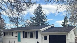 Une maison de plain-pied avec un garage, un porche à l’avant et une porte verte.