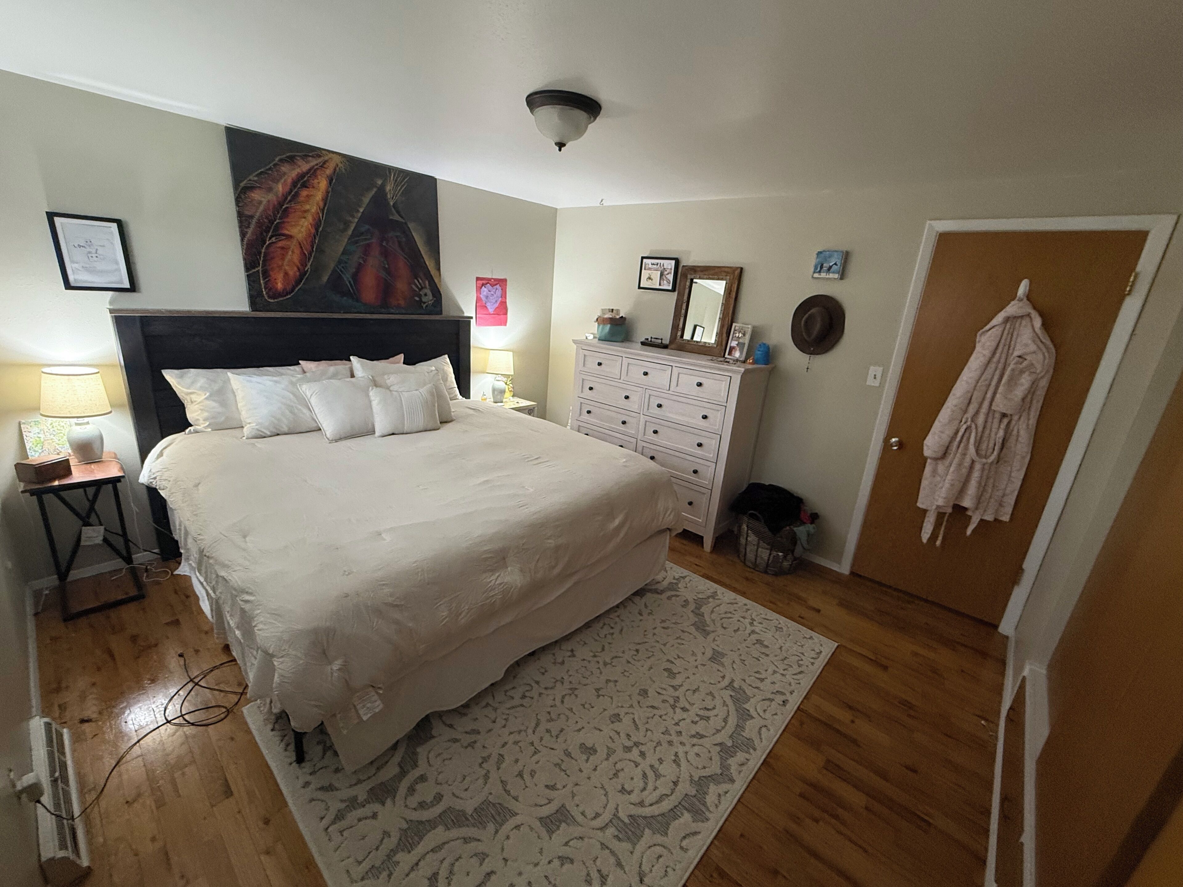 Una camera da letto con un letto grande, una cassettiera, un comodino, uno specchio fissato alla parete e una porta con un accappatoio appeso.