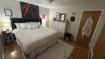 Una camera da letto con un letto grande, una cassettiera, un comodino, uno specchio fissato alla parete e una porta con un accappatoio appeso.