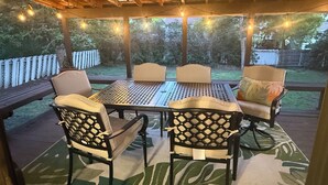 Une terrasse extérieure avec une table et des chaises, des guirlandes lumineuses et une vue sur le jardin.