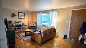 Un salon comprenant un canapé, une table basse, un bureau avec un ordinateur, une lampe et une fenêtre avec des rideaux.