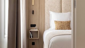 Una habitación de hotel con cama, mesita de noche, lámpara de pared y ventana con cortinas.