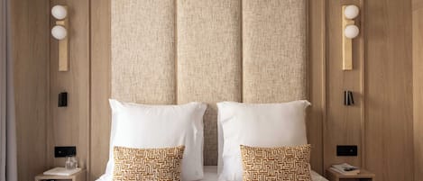 Een tweepersoonsbed met twee witte kussens en twee gestreepte kussens, een nachtkastje met een lamp en een wandlamp.