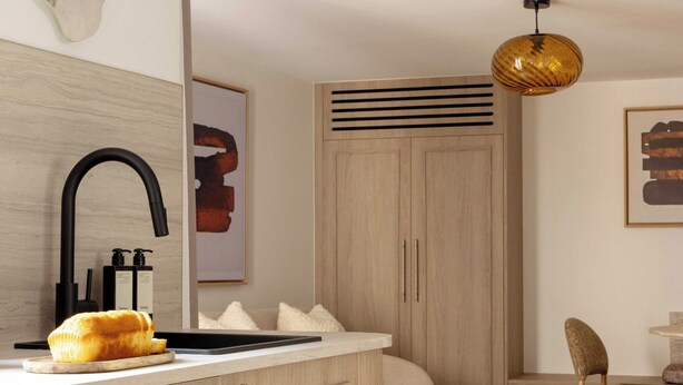 Una habitación de hotel moderna con un armario de madera, un grifo negro, una mesa redonda y una lámpara colgante.
