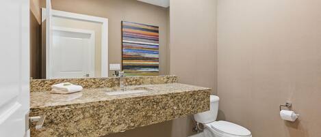 A bathroom with a granite countertop, a white toilet, and a wall-mounted towel dispenser.