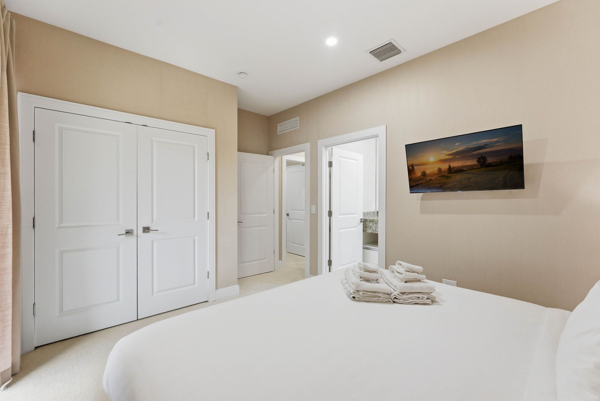 A hotel room with a large bed, a painting on the wall, and a closet with doors.
