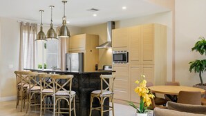 A modern kitchen with a central island, bar stools, and a dining area with a round table and chairs.