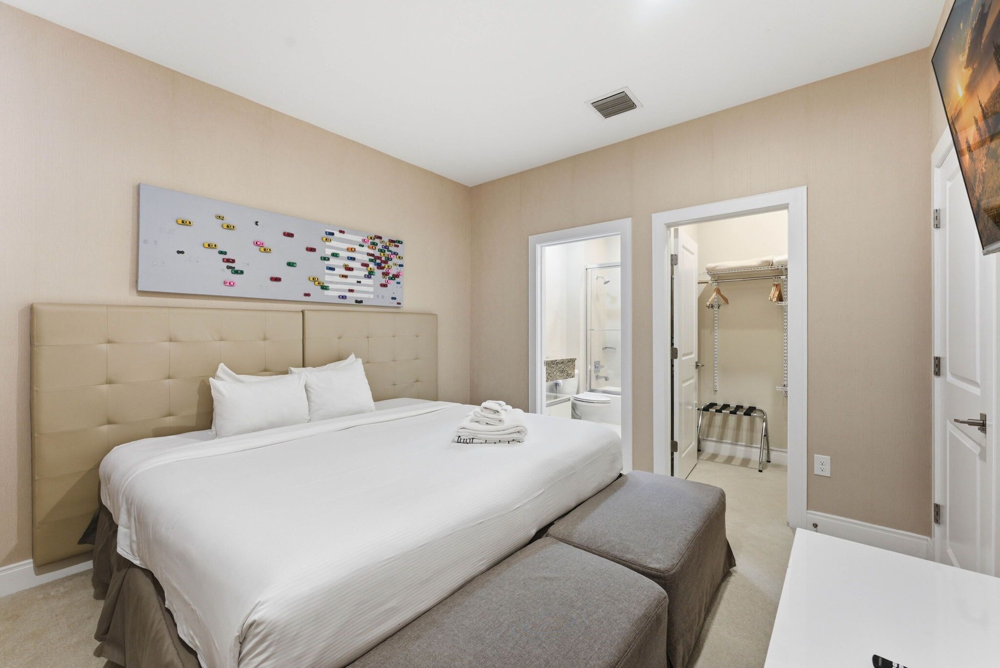 Ein Hotelzimmer mit einem großen Bett, einem Kopfteil, einem Wandbild, einem Kleiderschrank und einem durch eine offene Tür einsehbaren Badezimmer.